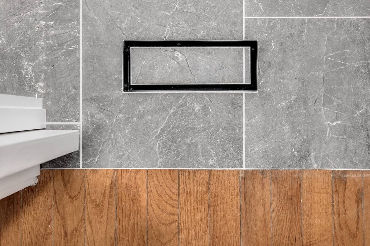 Sleek rectangular HVAC floor vent surrounded by gray stone tile and wood floor by Doxa Custom Homes, Middle Tennessee